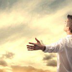 A man taking time alone to think, with his arms outstretched in front of a cloudy sky.