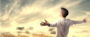 A man taking time alone to think, with his arms outstretched in front of a cloudy sky.