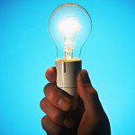 An illuminated light bulb grasped by a hand against a blue backdrop showcased in Gallery 1.