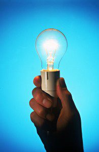 An illuminated light bulb grasped by a hand against a blue backdrop showcased in Gallery 1.