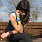 A woman sitting on a bench anxiously checks her phone, dreading a call from The Dreaded Telephone.