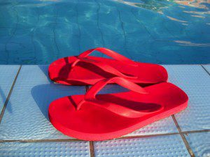 Red flip flops on the edge of a swimming pool during a vacation.