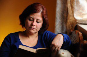 A woman taking time for herself, reading a book in front of a window.