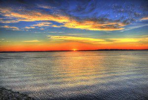 A majestic sunset serenely illuminating a vast water expanse, inspiring strength and resilience.