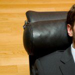A man in a suit is passively sleeping in an office chair.