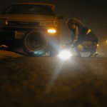 An introvert worries while putting a tire on a car at night.