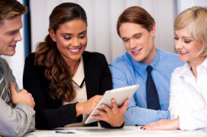 Four introverted business people analyzing data on a tablet during a meeting.