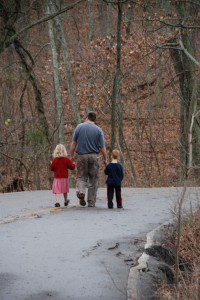 An introverted father and two children walking down a road in the woods.