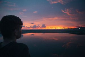 A man gazes at the sunset over a serene body of water.