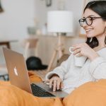 An introvert enjoying solitude in bed with a laptop and a cup of coffee.