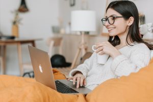 An introvert enjoying solitude in bed with a laptop and a cup of coffee.