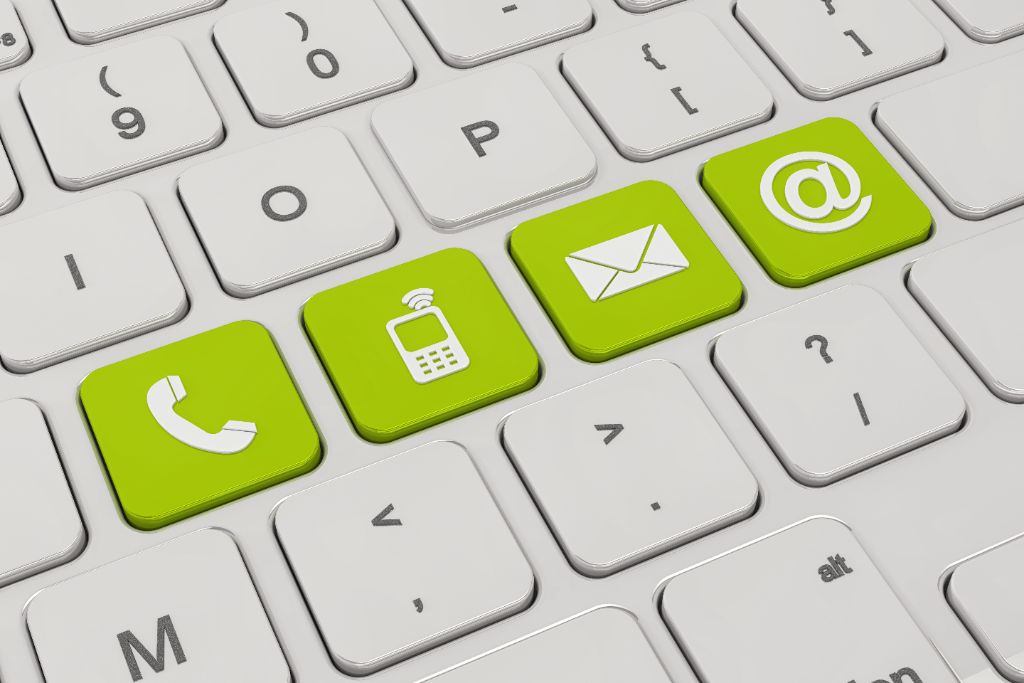 Close-up of a keyboard with green keys displaying contact icons: a telephone, a mobile phone, an envelope, and an "@" symbol. Reach out to us easily using these convenient keys.